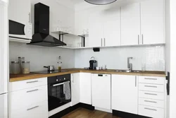 Белая кухня з драўлянай стальніцай і чорнымі ручкамі ў інтэр'еры